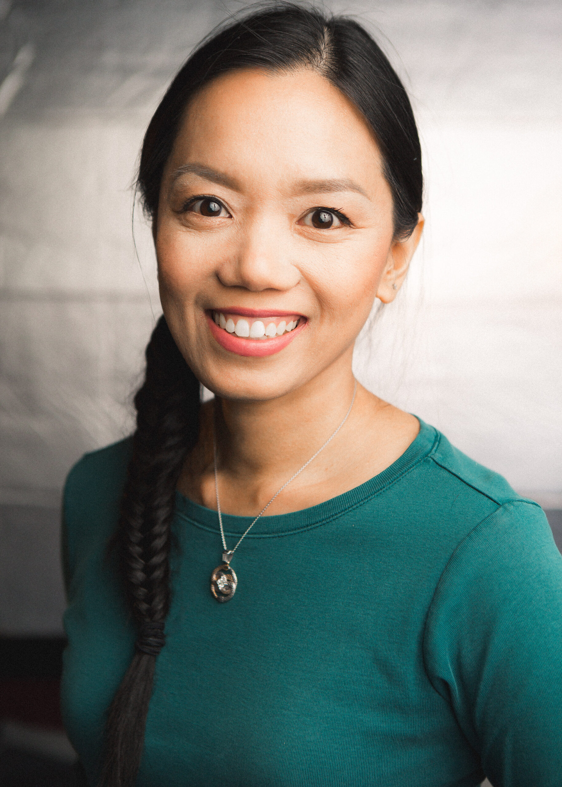 Veramarie is an olive-skinned woman who has her black hair in a side braid; she smiles with a teal green long-sleeved shirt